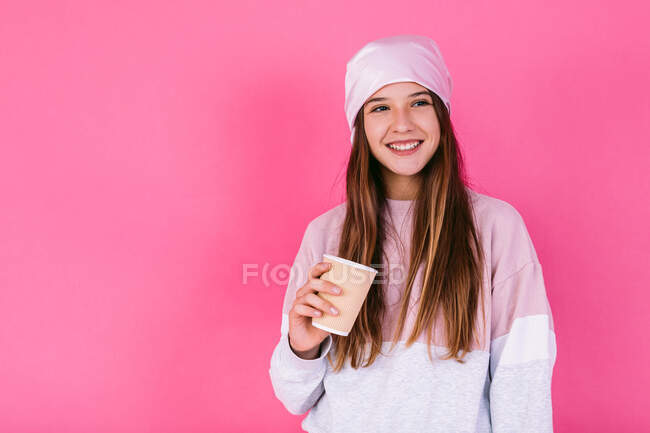 Feliz adolescente en pañuelo para la cabeza para el concepto de cáncer con una taza de papel de bebida caliente para llevar mirando hacia otro lado - foto de stock
