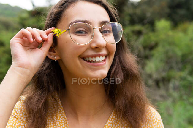 Allegro femmina con fiore selvatico giallo nei capelli guardando la fotocamera in campagna in estate — Foto stock