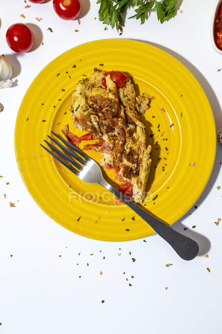 Deliciosa tortilla con perejil picado en plato contra tomates secados al sol sobre fondo blanco - foto de stock