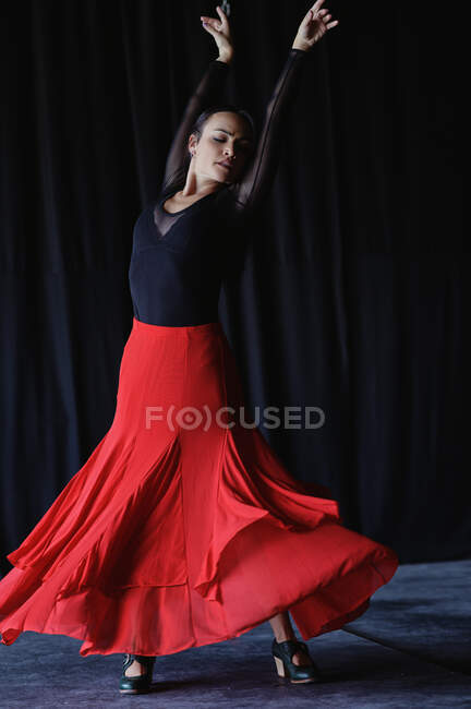 Young graceful woman in bright skirt and shoes dancing flamenco with raised arms on floor — Stock Photo