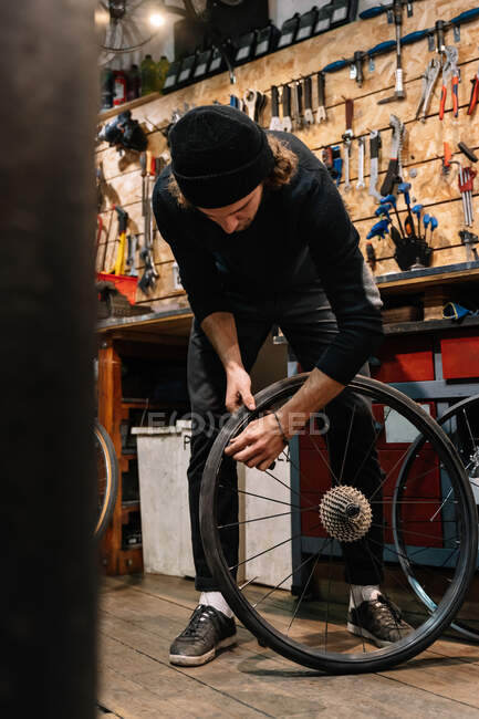 Baixo ângulo da roda de reparação mecânica masculina grave da bicicleta enquanto trabalhava na oficina — Fotografia de Stock