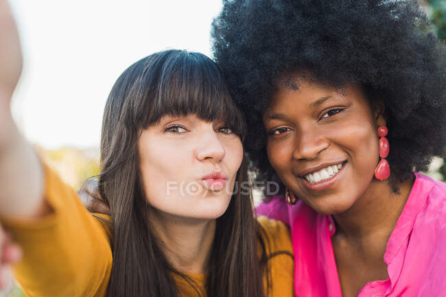Loving woman with black girlfriend while taking self shot in summer park and enjoying weekend — Stock Photo