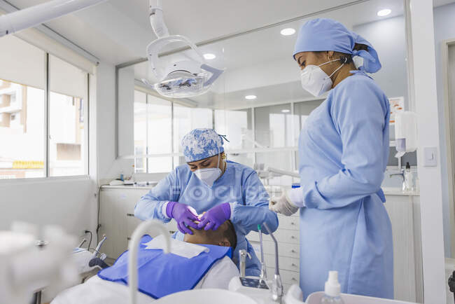 Женщина-стоматолог в униформе и респираторной маске вылечивает зубы пациентки мужского пола в больнице — стоковое фото