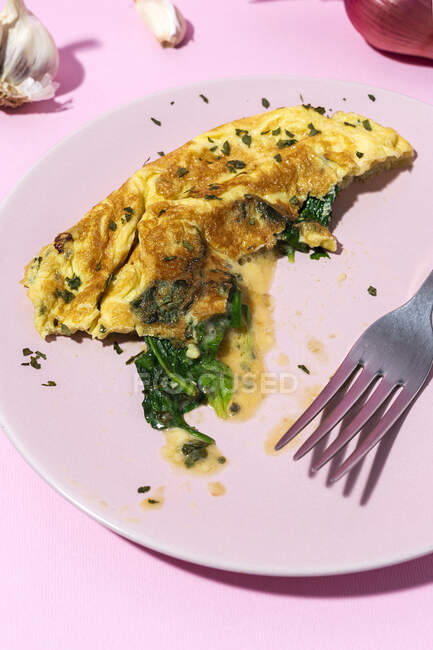 Leckeres Omelett auf Teller gegen frische Petersilienzweige und rote Zwiebel mit Knoblauchzehen auf rosa Hintergrund — Stockfoto