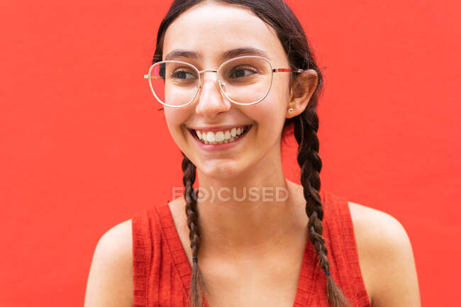 Jovem alegre no penteado pigtails enquanto olha para o fundo vermelho na rua — Fotografia de Stock
