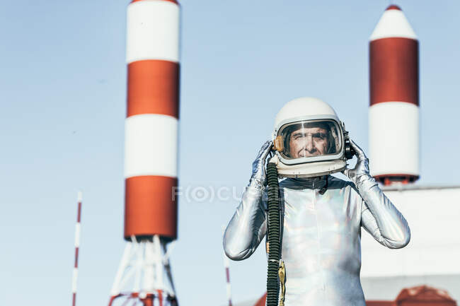 Homem em traje espacial em pé em solo rochoso contra antenas em forma de foguete listrado no dia ensolarado — Fotografia de Stock