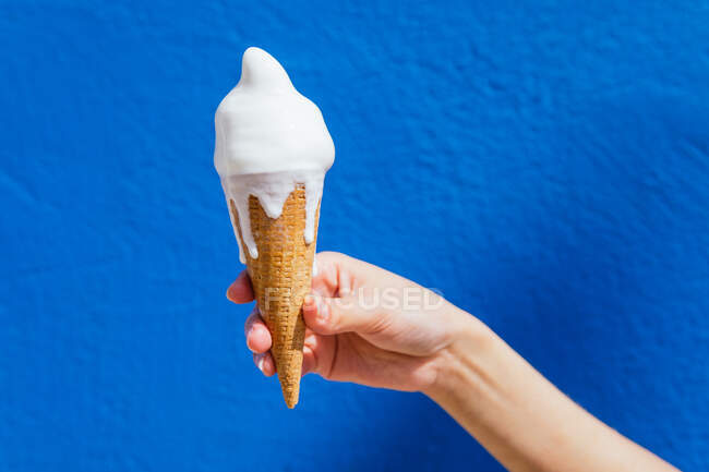 Mão de corte de fêmea anônima com sorvete derretendo em cone de waffle no dia ensolarado no fundo azul — Fotografia de Stock