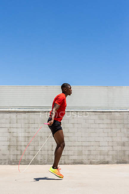 Вид сбоку на энергичного афроамериканского спортсмена, прыгающего с каната над землей во время тренировок летом — стоковое фото