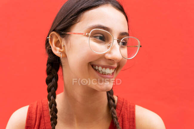 Веселая молодая женщина в косичках прическа, глядя в сторону на красный фон на улице — стоковое фото