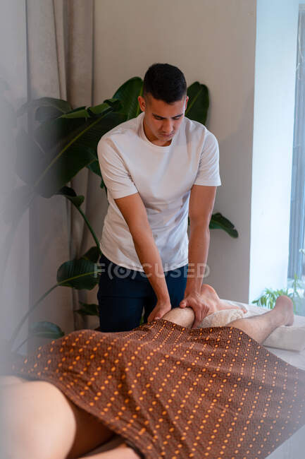 Terapeuta masaje piernas de cliente masculino mientras hace masaje tailandés en el centro de spa - foto de stock