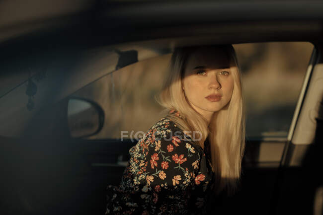 Portrait of a beautiful young pensive blonde woman sitting inside a car looking at camera at sunset — Stock Photo