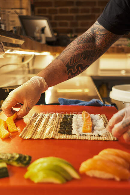 Cozinheiro irreconhecível preparando deliciosos rolos à mesa na cozinha no restaurante japonês — Fotografia de Stock