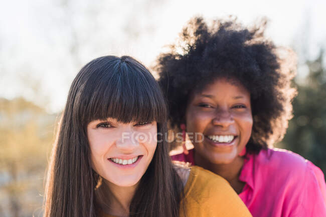 Multiethnic couple of homosexual embracing while smiling looking at camera on sunny day in park — Stock Photo