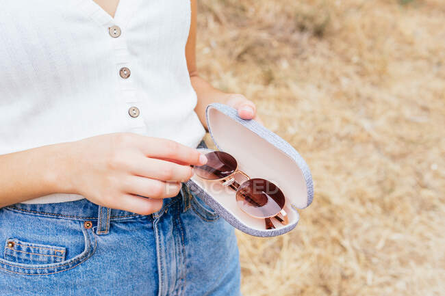 Side view of anonymous woman putting sunglasses in a case while holding it in her hands — Stock Photo