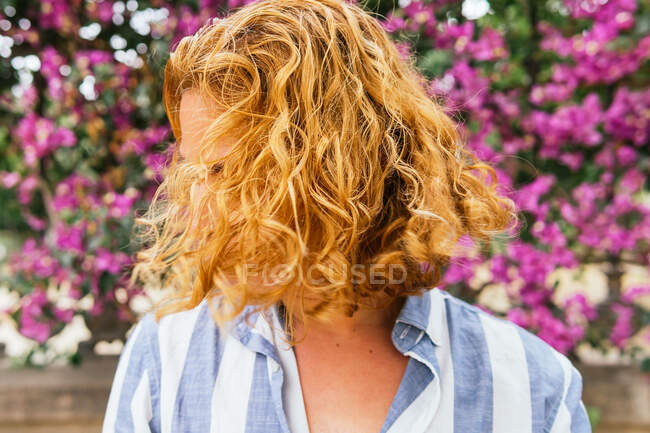 Мрійливий допитливий чоловік з довгим хвилястим літаючим волоссям, що стоїть на вулиці влітку в парку під квітучим деревом з рожевими квітами — стокове фото
