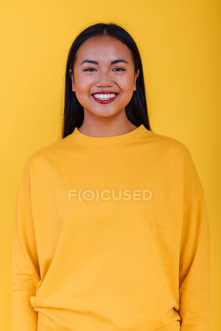 Delighted Asian female standing on yellow background in studio while looking at camera — Stock Photo