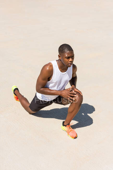 Fit afroamerikanischer männlicher Athlet bei Ausfallgymnastik und Stretching der Beine beim Aufwärmen während des Trainings an sonnigen Sommertagen — Stockfoto