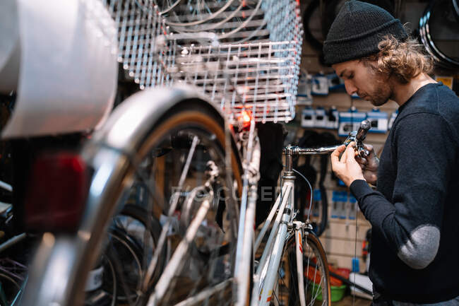 Seitenansicht eines geschäftigen männlichen Meisters, der sein Fahrrad repariert, während er in einer schäbigen Reparaturwerkstatt arbeitet — Stockfoto