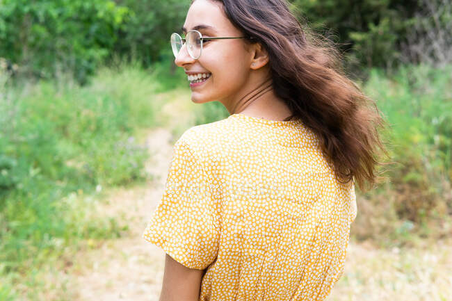 Вид сзади восхищенной женщины в платье, гуляющей в парке и отводящей взгляд через плечо летом — стоковое фото