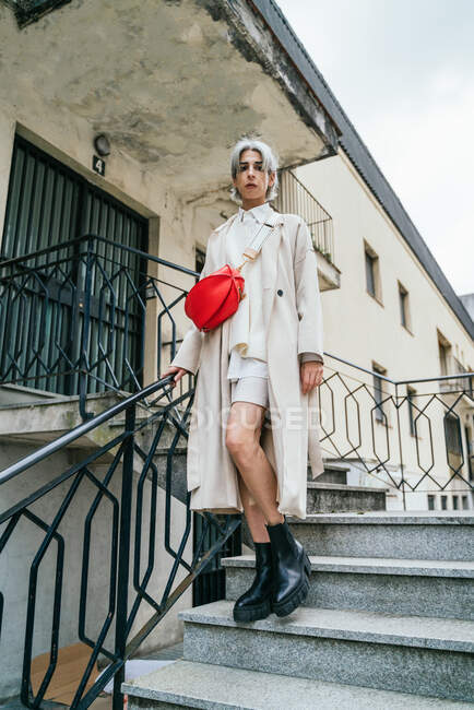 Self assicurato transgender femminile in abiti eleganti e con i capelli grigi in piedi nelle scale guardando la fotocamera in zona urbana in città — Foto stock