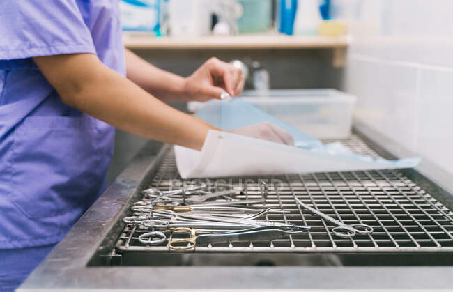 Побічний вигляд врожаю невизначений ветеринарний лікар з металевими пінцетами в руці готує інструменти для хірургічного втручання у ветеринарній лікарні — стокове фото