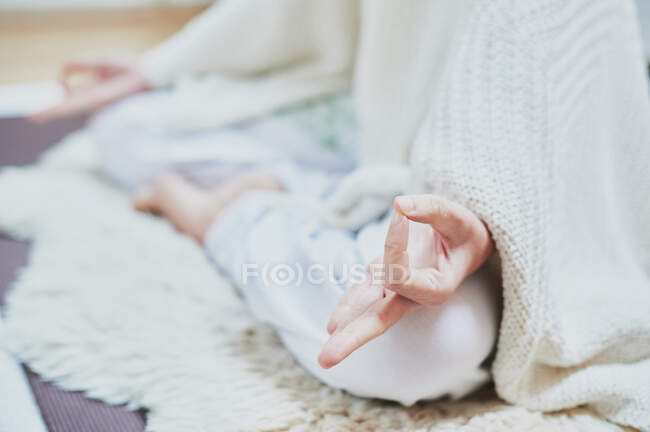 Crop femelle anonyme assis avec les jambes croisées sur tapis moelleux tout en pratiquant le yoga dans la chambre — Photo de stock