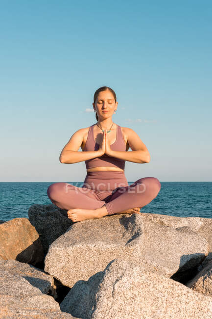 Спокойная женщина с закрытыми глазами, занимающаяся йогой в позе Лотоса во время медитации на скале на берегу моря — стоковое фото