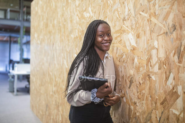 Femme entrepreneur afro-américaine souriante debout avec tablette près du mur dans l'espace de coworking tout en regardant la caméra — Photo de stock