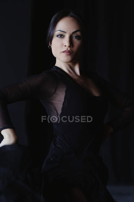 Young graceful woman in black wear dancing flamenco with raised arms while looking at camera — Stock Photo