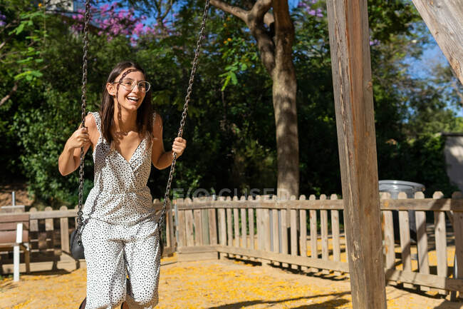 Веселая молодая женщина в очках качается в парке в солнечный летний день — стоковое фото