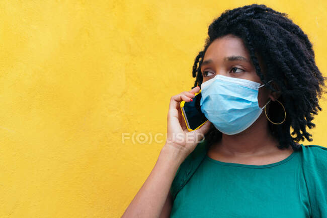 Porträt einer jungen Frau mit Schutzmaske, die auf der Straße mit dem Smartphone spricht. Pandemiekonzept — Stockfoto