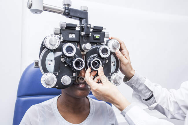 Optometrista ajustando el equipo de optometría durante el estudio de la vista de una mujer negra - foto de stock
