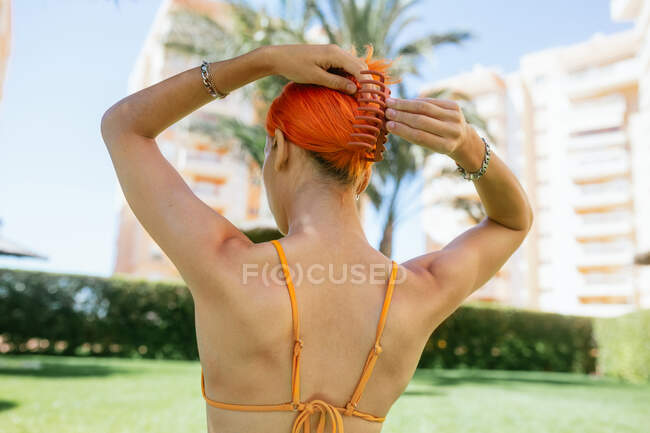 Back view of anonymous young redhead woman making a ponytail at holidays resort on a sunny day in summer — Stock Photo