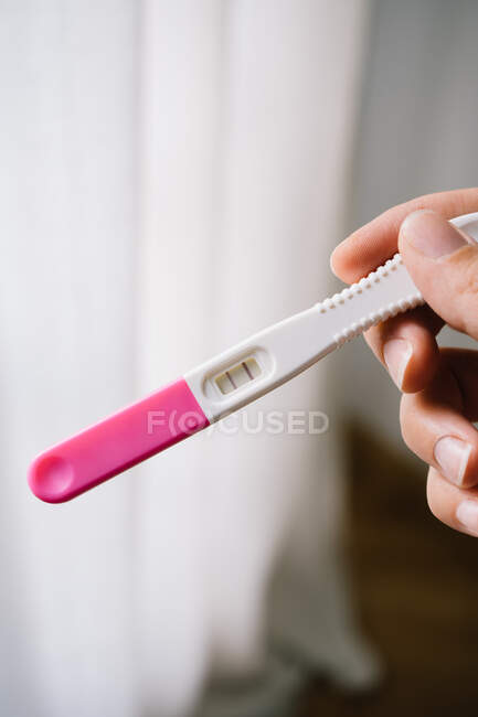 Cortado mãos mulher irreconhecível segurando um teste de gravidez além de uma janela — Fotografia de Stock