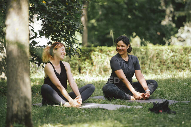 Вміст весела доросла краща жінка друзі спілкуються після практики йоги в сонячному світлі, сидячи на килимках йоги — стокове фото
