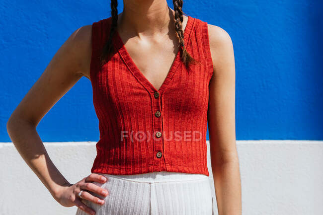 Cropped unrecognizable female in pigtails hairstyle standing with hands on waist on blue background in street — Stock Photo