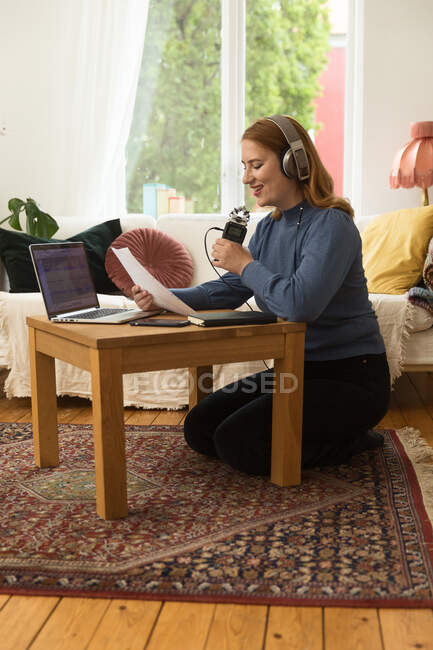 Encantado anfitrião de rádio feminino gravação podcast ao usar microfone e ler notas de papel em casa — Fotografia de Stock
