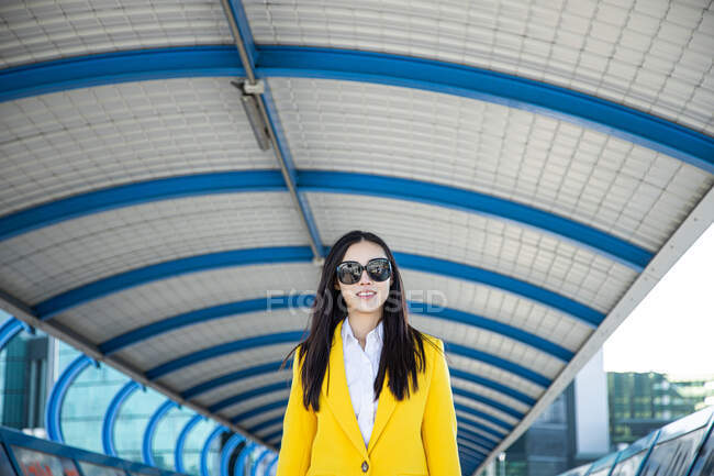 Усміхнена азіатська бізнес-леді з жовтим пальто ходьби на злітному смузі — стокове фото