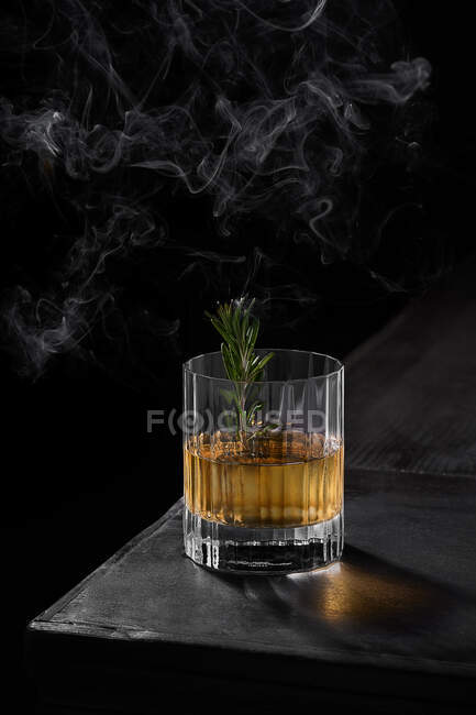 From above glass of cold whiskey decorated with green leaf placed on black table in dark smoky room — Stock Photo