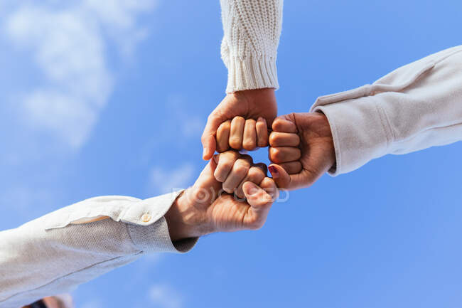 From below of faceless close friends bumping fists against clear blue sky in sunlight — Stock Photo