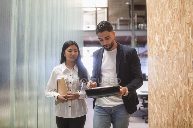 Serious multiracial male and female coworkers using tablet and discussing business project in modern coworking space — Stock Photo