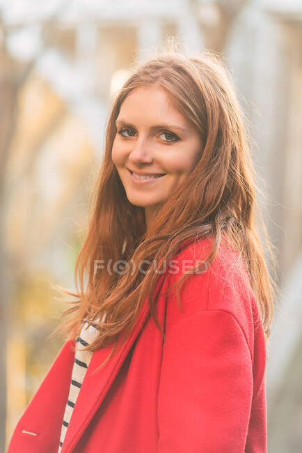 Contenu charmante jeune femme debout dans le parc à l'automne et regardant la caméra — Photo de stock