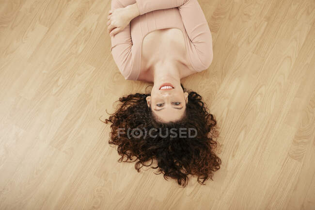 From above of tender female in beige bodysuit lying on wooden floor and looking at camera — Stock Photo