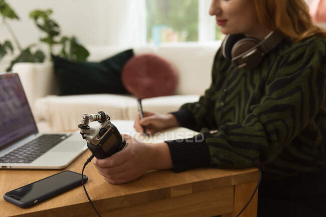 Вид збоку на обрізаний невідомий фокусований жіночий радіоведучий з мікрофоном і навушниками, що пишуть в блокноті, готуючись до запису подкасту вдома — стокове фото