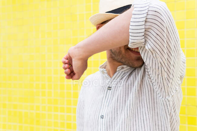 Unbekannter in stylischem Sommeroutfit und Hut macht keine Geste und versteckt Gesicht vor Kamera gegen gelbe Wand — Stockfoto