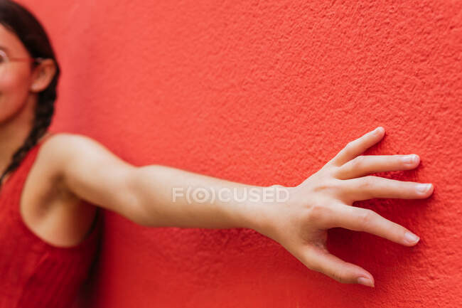 Side view of cropped unrecognizable female leaning on red wall of building in street with outstretched arm — Stock Photo