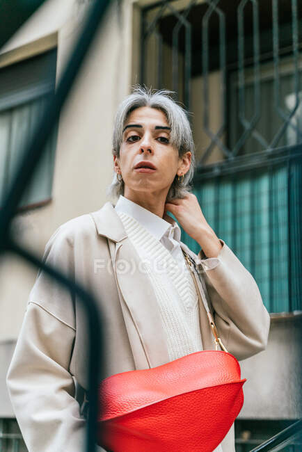 Самоуверенная трансгендерная женщина в стильной одежде и с седыми волосами, смотрящая в камеру в городской зоне города — стоковое фото