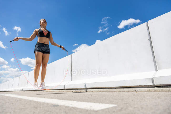 Giovane donna che si allena con la corda da salto all'aperto, vista laterale — Foto stock