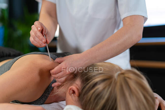 Unerkennbarer Physiotherapeut steckt Nadel in Schulter entspannter Patientin während Akupunktur-Sitzung in Klinik — Stockfoto