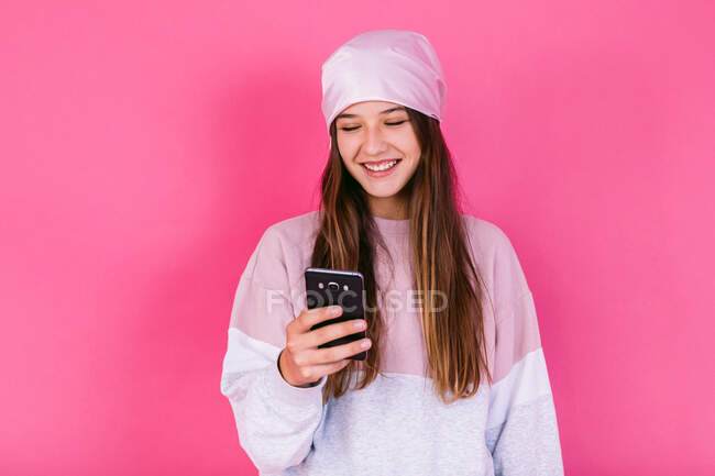 Happy female adolescent with brown hair in headscarf for cancer concept awareness browsing on cellphone — Stock Photo